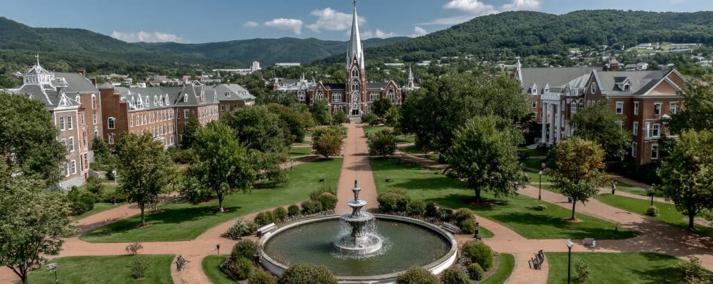 Aerial view of a college campus with a central fountain, red-brick paths, trees, and mountains in the background.